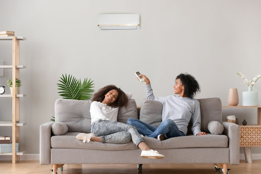 Two women sitting on the couch enjoying cool air coming from their ductless mini-split.