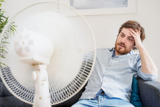 A man sitting on a couch in front of a fan.