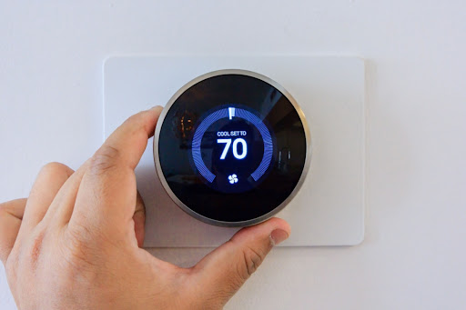 A hand touching a smart thermostat that reads, "cool set to 70."