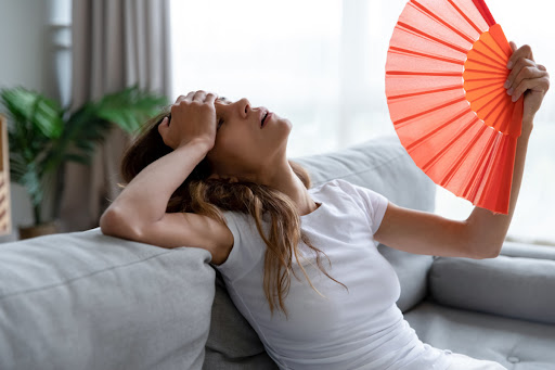An exhausted-looking woman fanning herself with a hand fan as she sits on a couch.