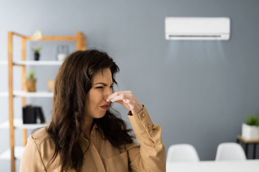A woman holding her nose due to a bad air conditioner smell.