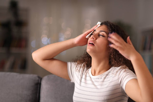 A woman fanning herself and putting a cool cloth on her head because her house is hot.