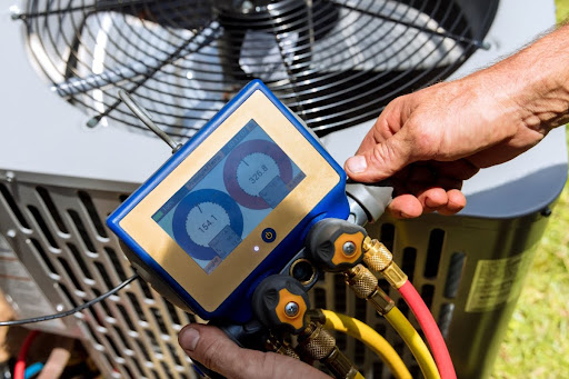 A close-up of a man's hands as he uses equipment and performs a service on a central air conditioning unit.